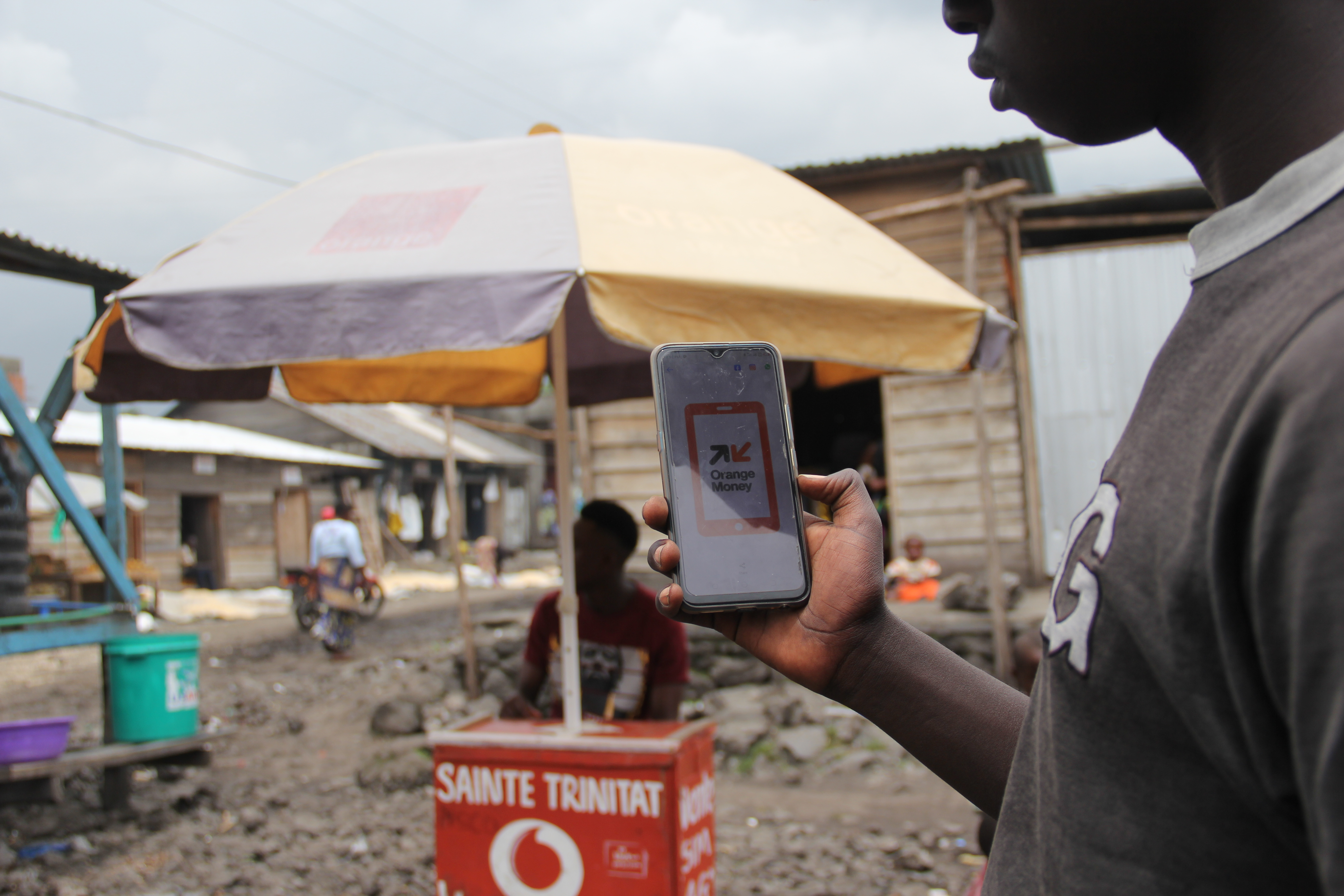 Congolese man displays phone with cash distribution app. 