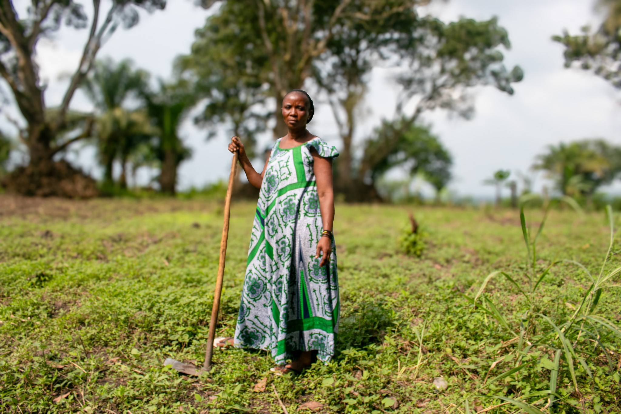 Woman standing in agricultural setting holding farming implement.