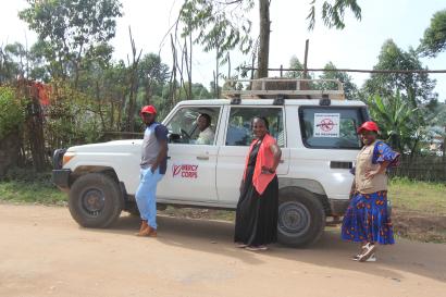 Mercy corps employees stand, smiling, in front of a vehicle.