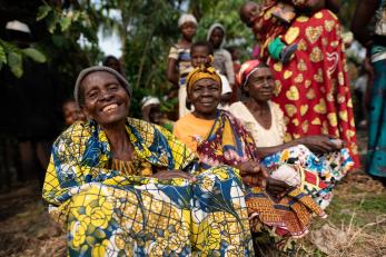 Congolese community members sitting outside in colorful clothing, smiling.