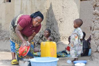 Woman washing cookware outside as family looks on.