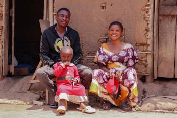Family of three sit outside their home, smiling.