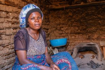 Drc woman sitting in her living space, with cooking pot in background.