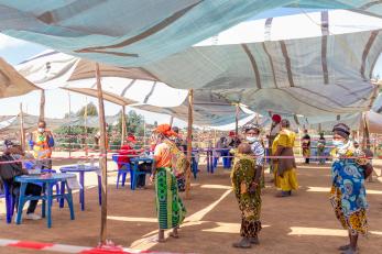 Drc individuals during cash assistance program event, in line, under tent.