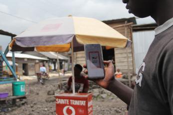 Congolese man displays phone with cash distribution app. 