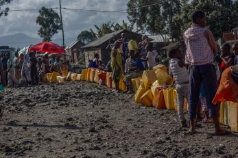 Adults and children wait along a line of jerry cans in Goma.