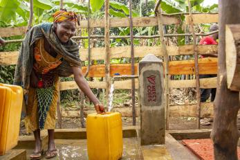 A person smiles while filling up a jerry can with water from a spigot.
