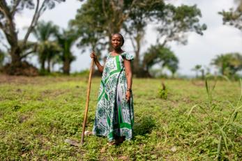 Woman standing in agricultural setting holding farming implement.