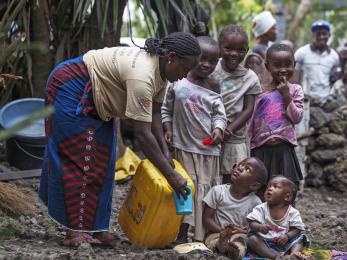 A woman pouring water for children in drc