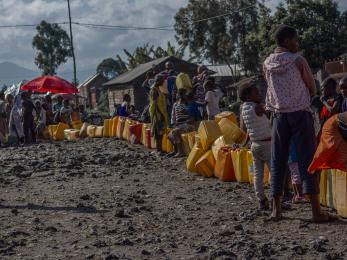 Adults and children wait along a line of jerry cans in goma.