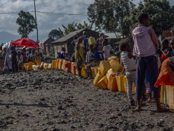 Adults and children wait along a line of jerry cans in Goma.