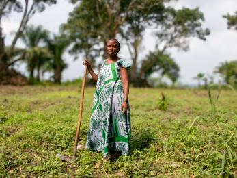 Woman standing in agricultural setting holding farming implement.
