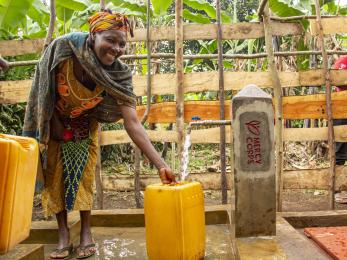 A person smiles while filling up a jerry can with water from a spigot.
